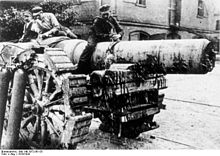 three men sit on top of a large artillery piece.