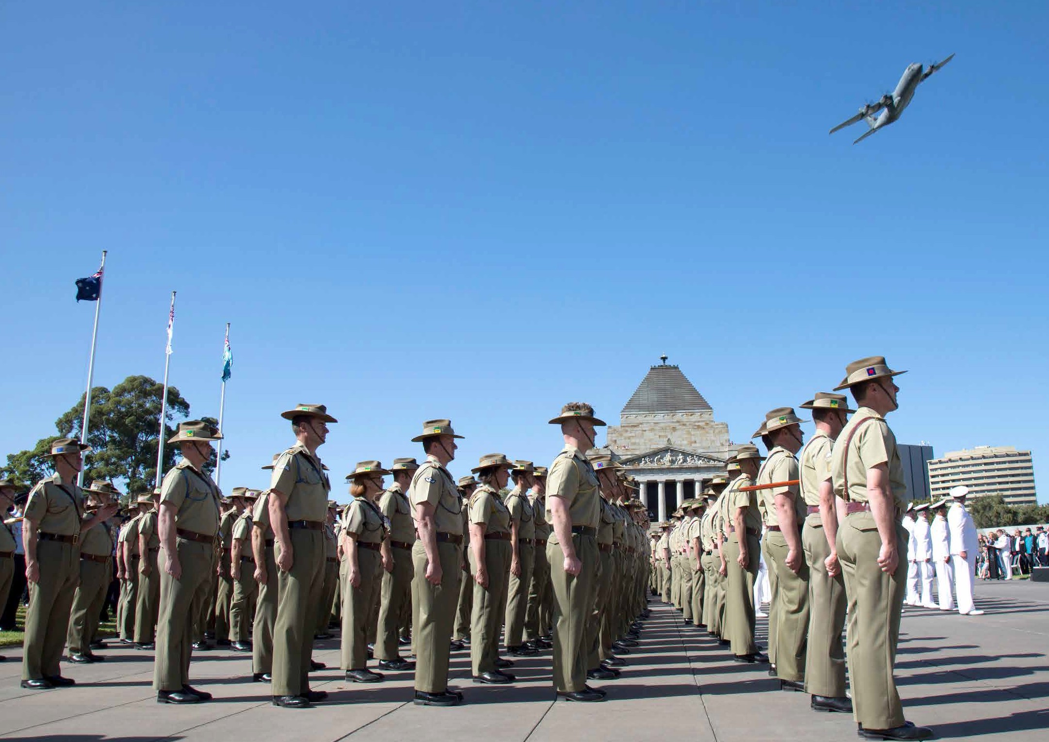 soldiers in formation outside the shrine of rememberance with a plane flying overhead.